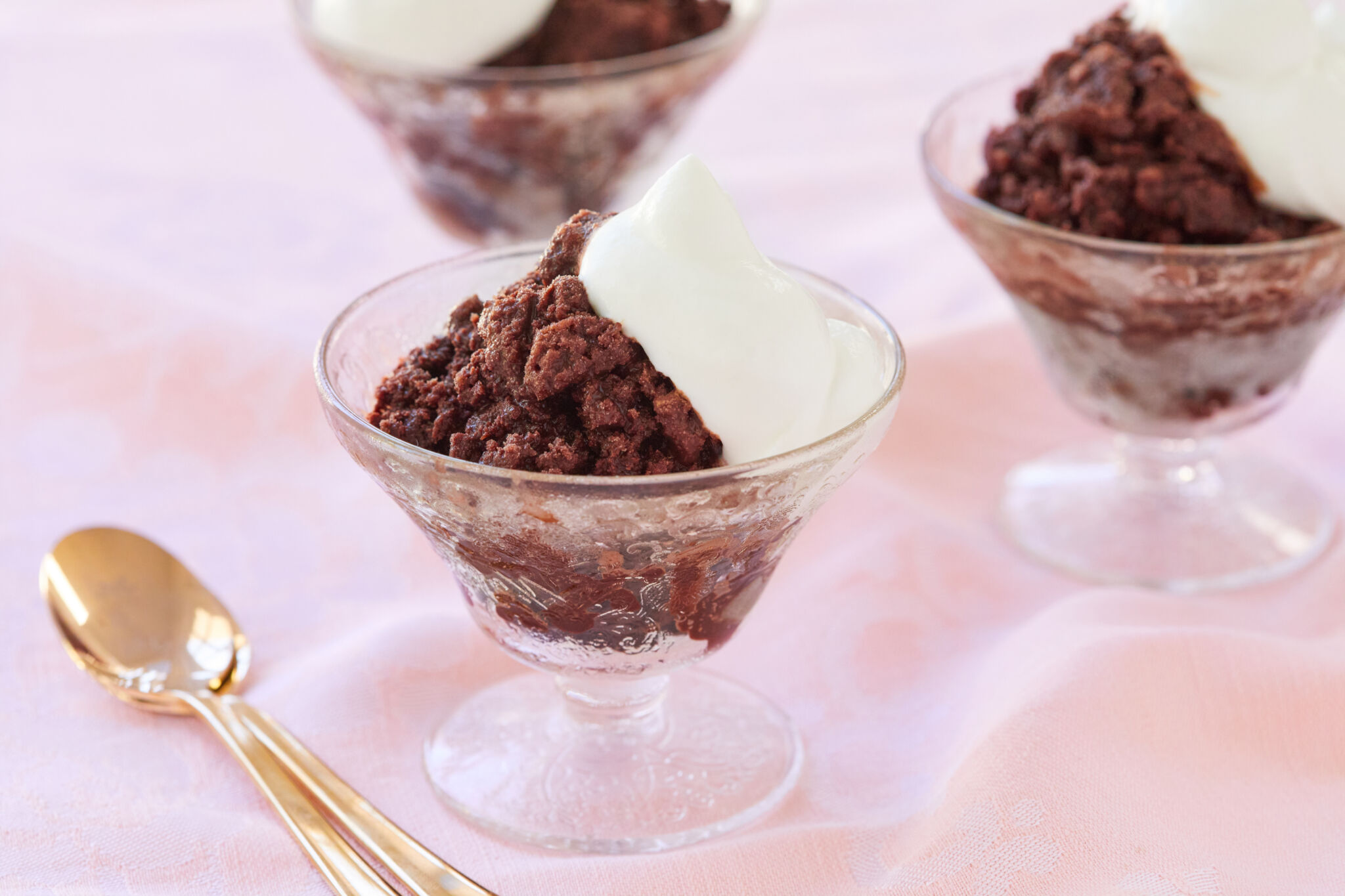 The crunchy semi frozen dessert Chocolate granita is served in 3 clear textured glass ice cream cups with perfectly whipped cream on top. A golden spoon in the left bottom corner.
