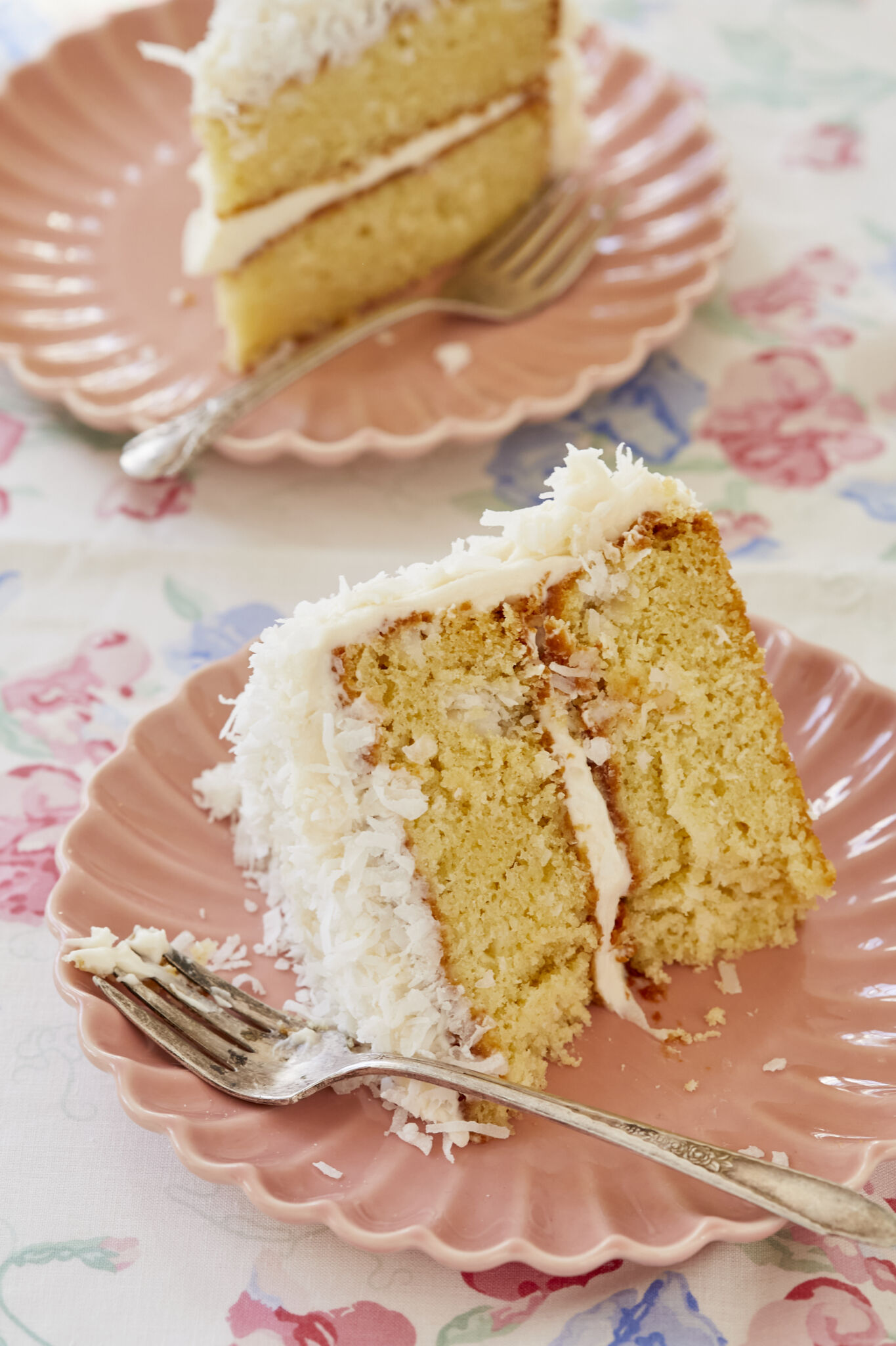 Two slices are served with fork on the plates, showing very moist and soft crumb, smooth frosting and crunchy flakes. . 