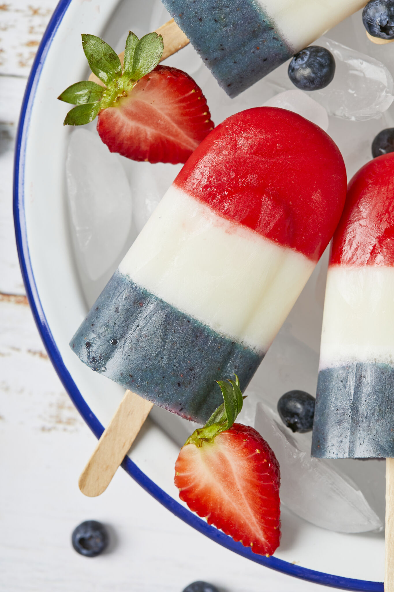 Bomb pops are served on half of the platter with ice and fresh blueberries and strawberries. 