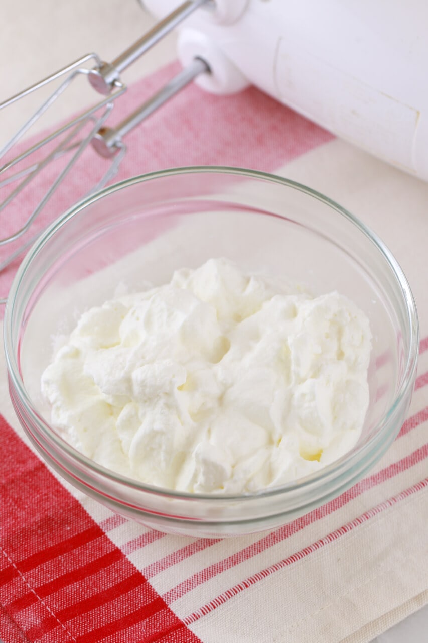 Softly whipped heavy whipping cream in a glass bowl with hand-handled electric mixer on the side. Heavy Whipping Cream is the base of the Easiest Homemade Ice Cream Recipe and aerates the ice cream to make it light. 