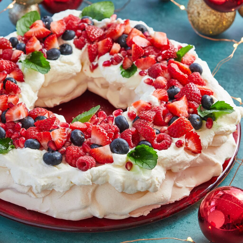 The gorgeous Christmas Wreath Pavlova has marshmallow like white crunchy exterior and marshmallow-like center . It's crowned with freshly whipped cream, and fresh colorful fruits including strawberries, raspberries, blueberries and green leaves for color contrast.
